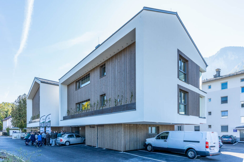 Neue Mietwohnungen in Grödig: Wohnhaus mit Holzfassade und Fassadenbegrünung, davor Gäste bei der Übergabe am 20. Oktober 2026