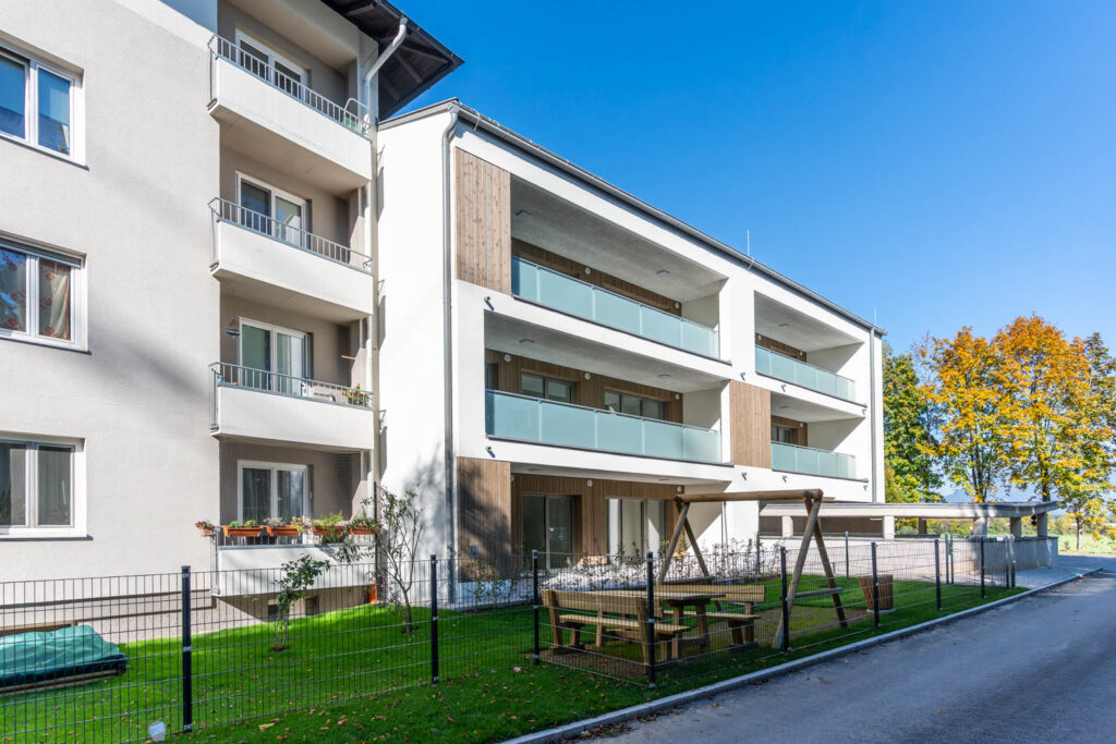 Neues Wohnhaus der Wohnbau Bergland in der Hauptstraße 2 in Grödig mit Glasbalkonen, Kinderspielplatz und Sitzgarnitur im Garten